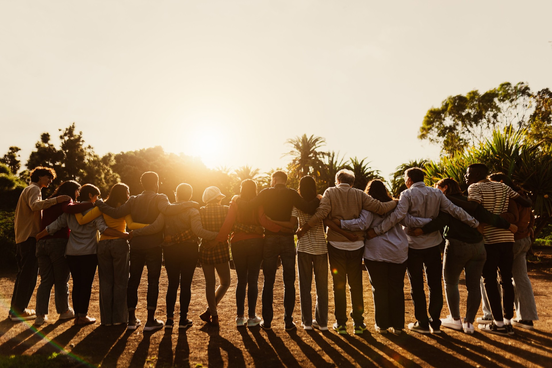 Vista trasera de personas multigeneracionales felices divirtiéndose en un parque público durante la puesta del sol - Concepto de comunidad y apoyo
